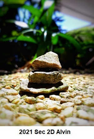 Small stack of rocks balanced on a pebble-covered ground with blurred greenery in the background.